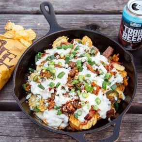 Nachos with steak and beer-cheese sauce in a cast iron skillet. Bag of kettle chips and can of beer in frame.