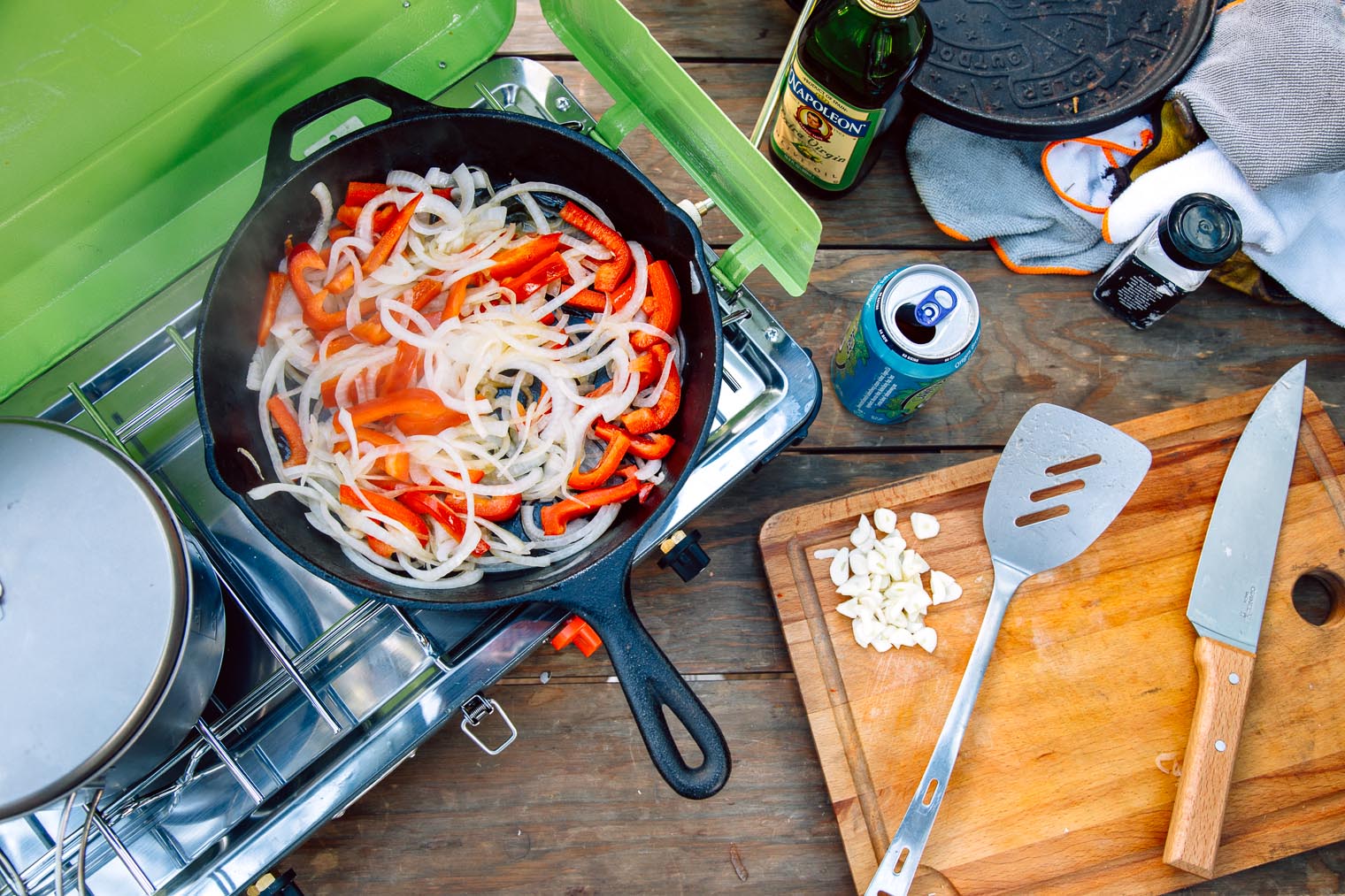 Onions and red bell peppers cooking in a cast iron skillet over a camping stove