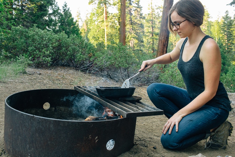 Megan using a cast iron skillet to cook over a campfire