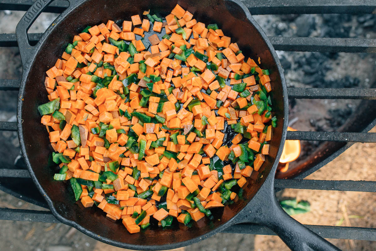Sweet potatoes and green peppers cooking in a cast iron skillet