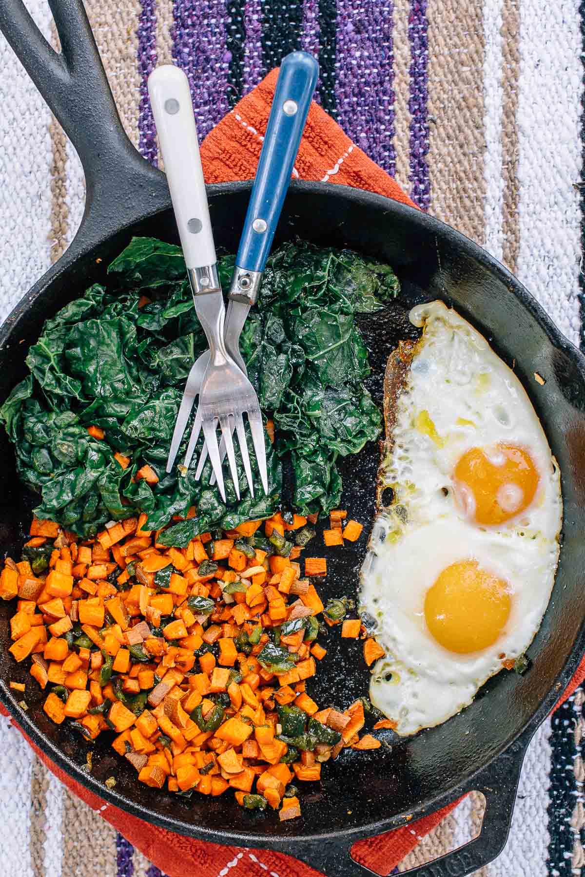 A cast-iron skillet with kale sweet potato and two eggs