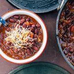 5 can chili in a red and white camping bowl next to a Dutch oven.