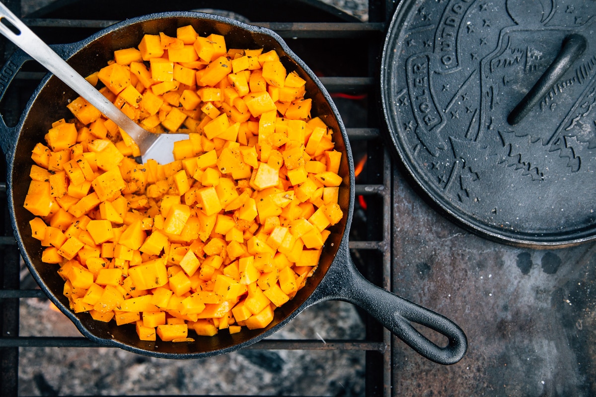 Butternut squash in a cast iron skillet cooking over a campfire