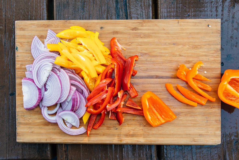 Sliced onions and peppers on a wooden cutting board