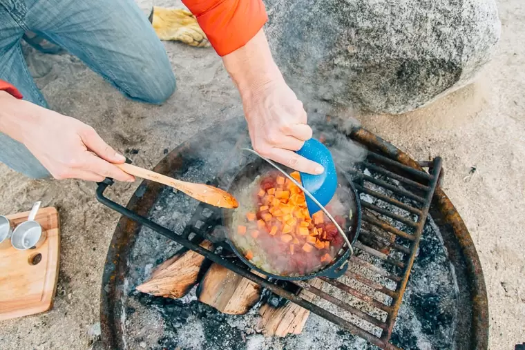 Michael adding chopped sweet potatoes into a Dutch oven that is on a campfire