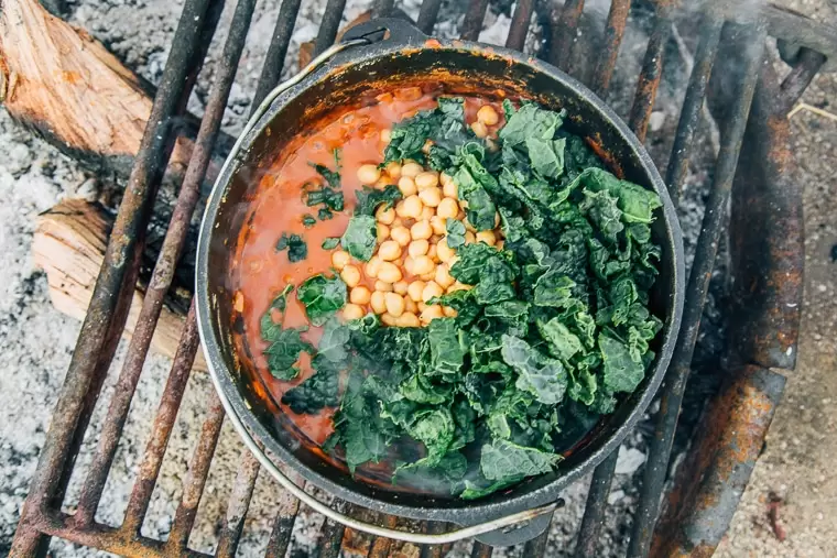 Chickpeas and kale in a Dutch oven stew on a campfire