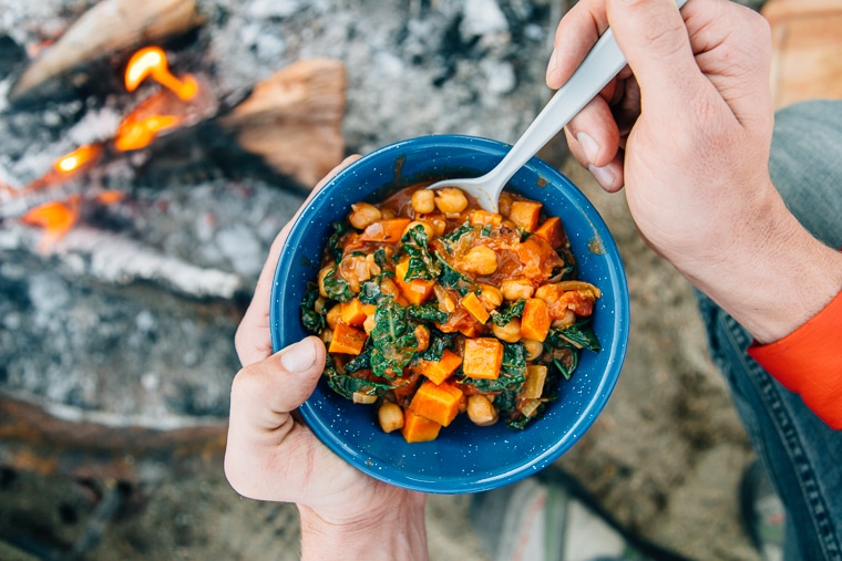 Sweet potato peanut stew in a blue camping bowl in front of a campfire.
