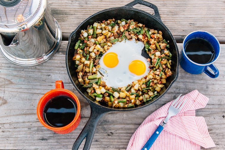 Breakfast hash with two eggs in a cast iron skillet on a wooden camping table