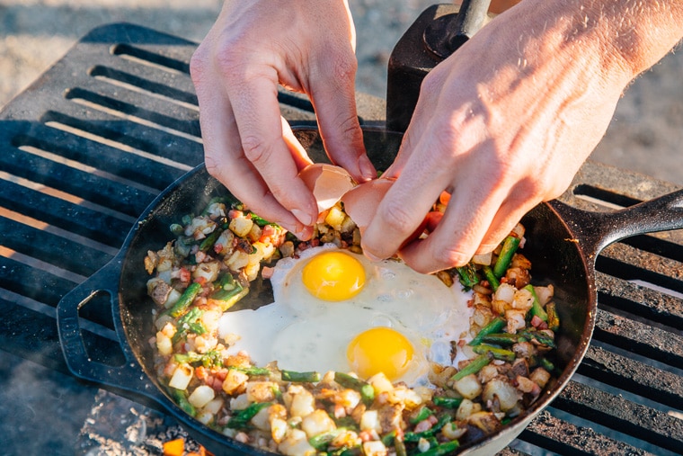 Michael cracking eggs into a cast iron skillet full of breakfast hash