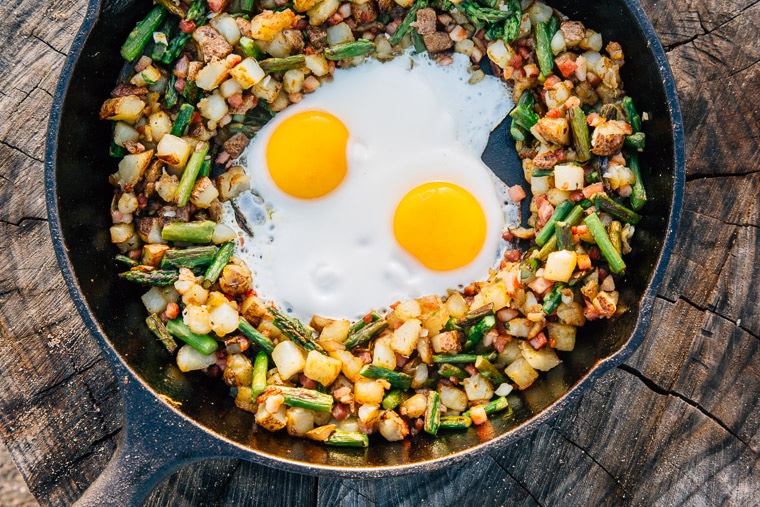 Breakfast hash with two eggs in a cast iron skillet on a wood stump