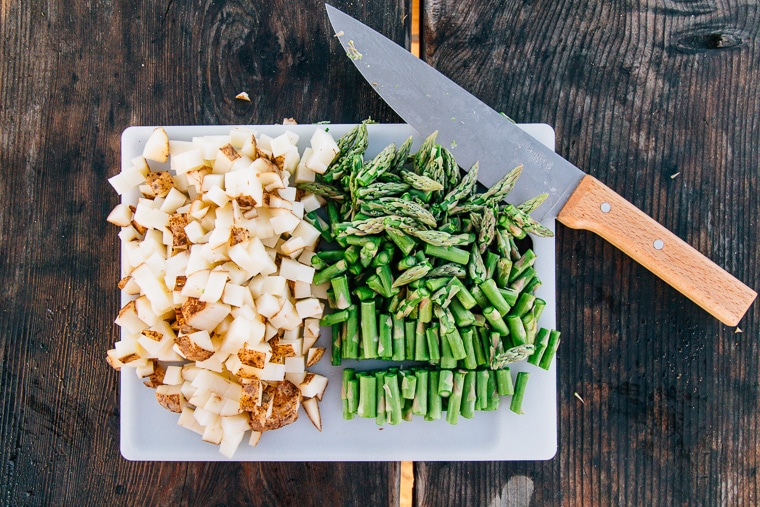 Potatoes and asparagus cut up on a cutting board