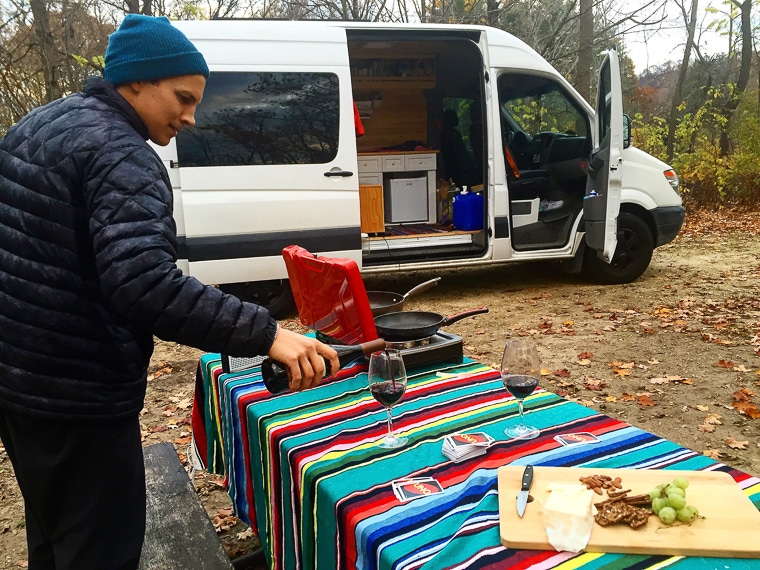 A man pouring a glass of red wine at a camp table in front of a sprinter van