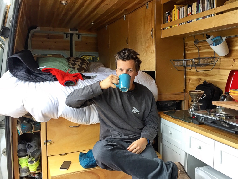 A man drinking from a cup of coffee inside a sprinter camper van