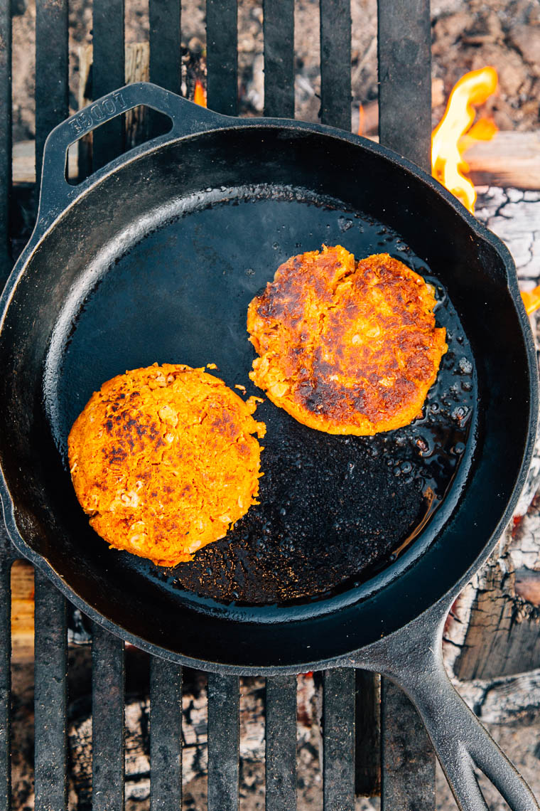 Two sweet potato and bean burgers in a cast iron skillet over a campfire