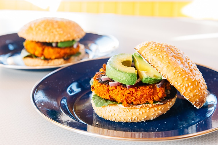 Two sweet potato bean burgers topped with avocado on blue plates