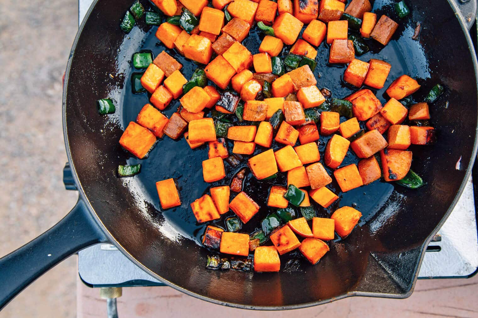 Peppers and sweet potatoes frying in a cast iron skillet