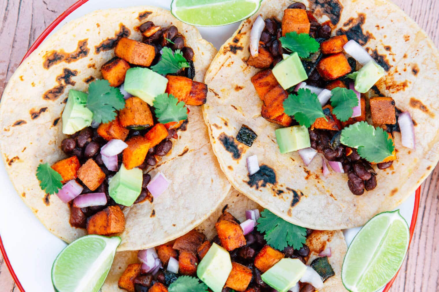 Tacos filled with sweet potatoes and black beans on a red and white plate