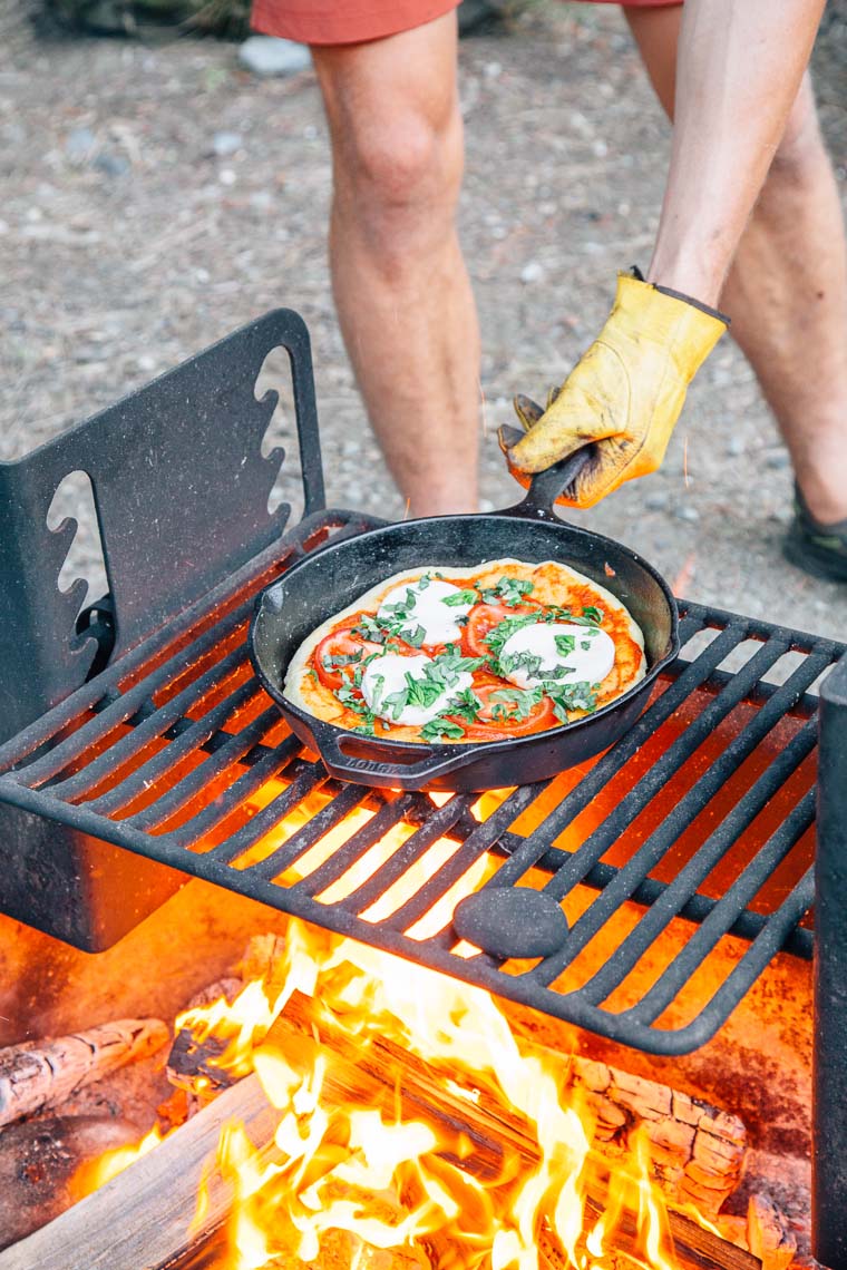 Michael placing a cast iron skillet pizza over the campfire