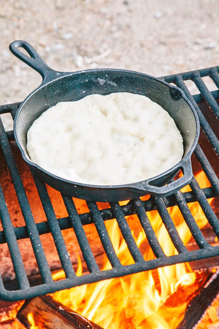 Pizza dough cooking in a cast iron skillet over a campfire