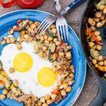 Chickpea hash with two eggs on a blue plate next to a cast iron skillet