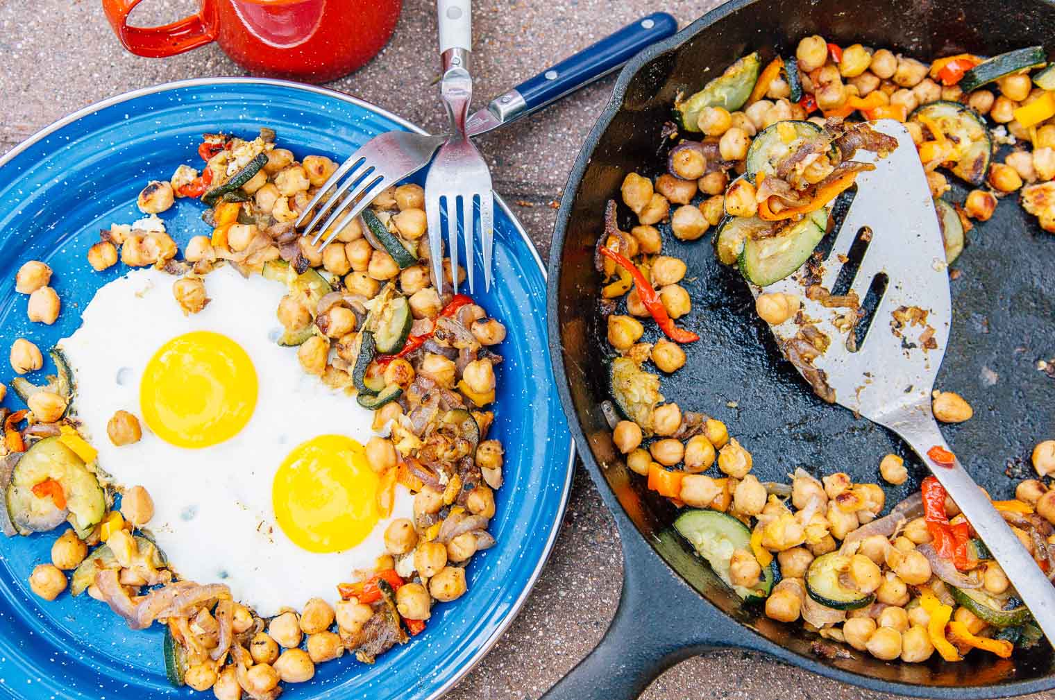 Breakfast hash on a blue enamelware camping plate next to a cast iron skillet