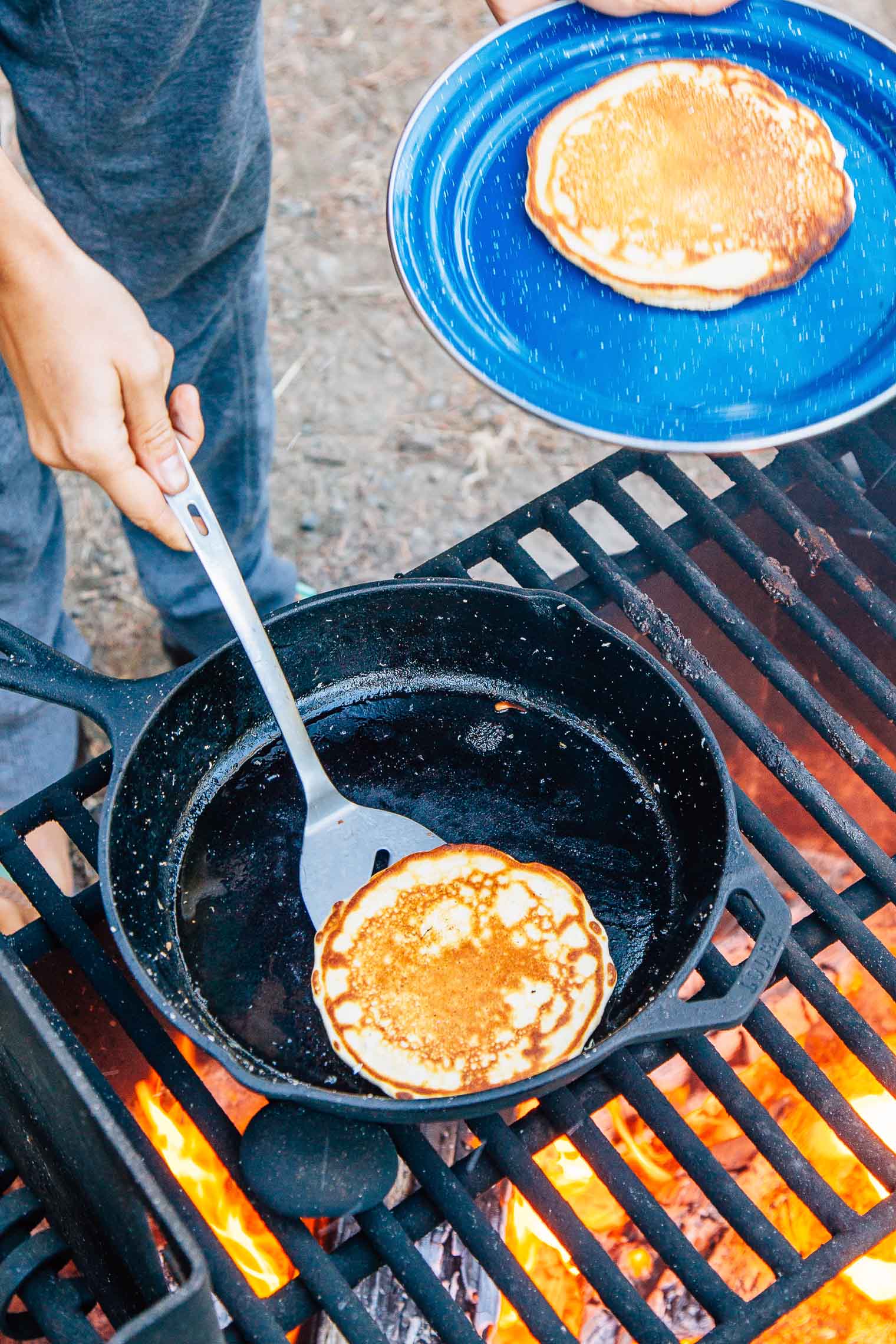 Michael using a spatula to remove a pancake from a cast iron skillet over a campfire