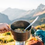 Michael holding a backpacking pot filled with ramen with mountains in the distance