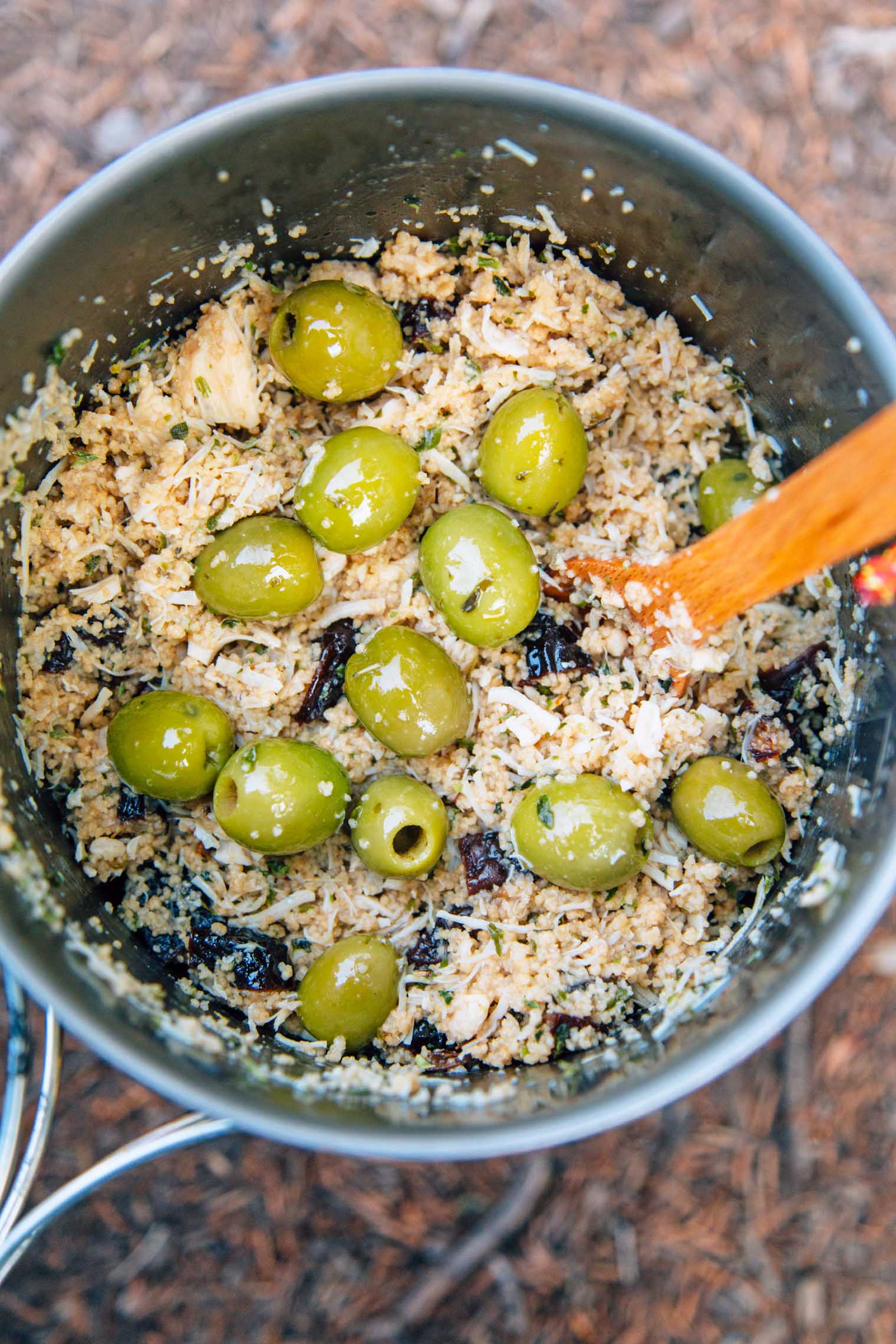 A wooden spoon in a pot that is filled with couscous and green olives
