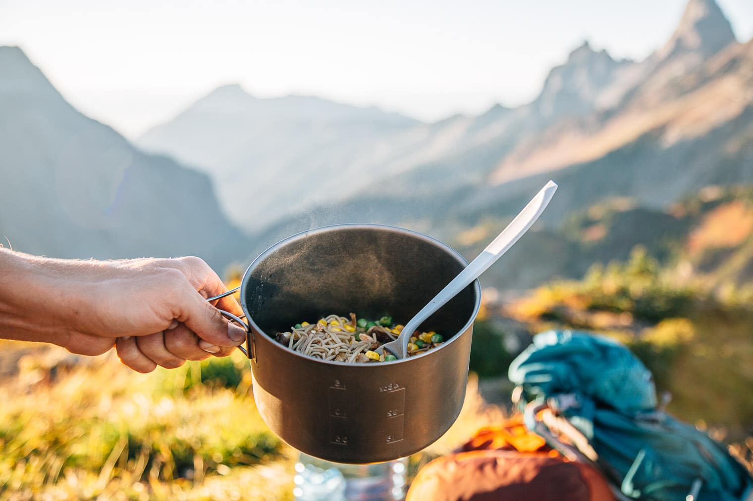 Michael holding a backpacking pot filled with ramen with mountains in the distance