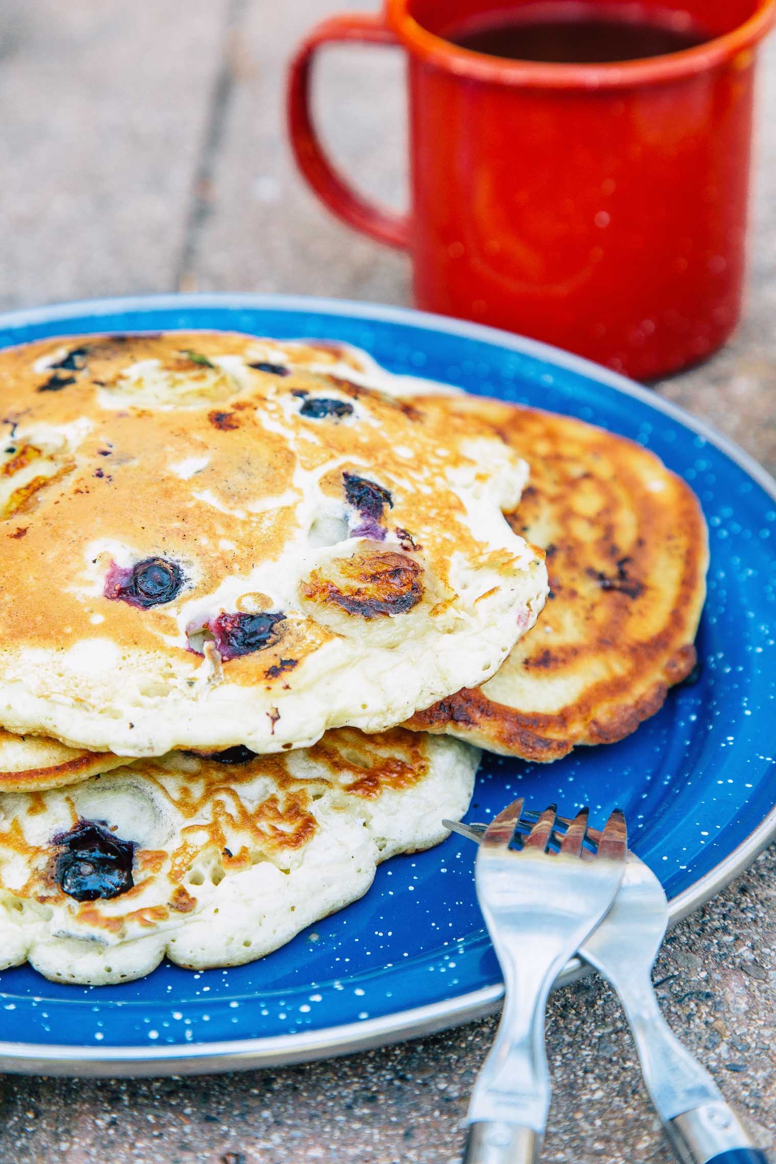 A stack of blueberry banana pancakes on a plate next to a cup of coffee