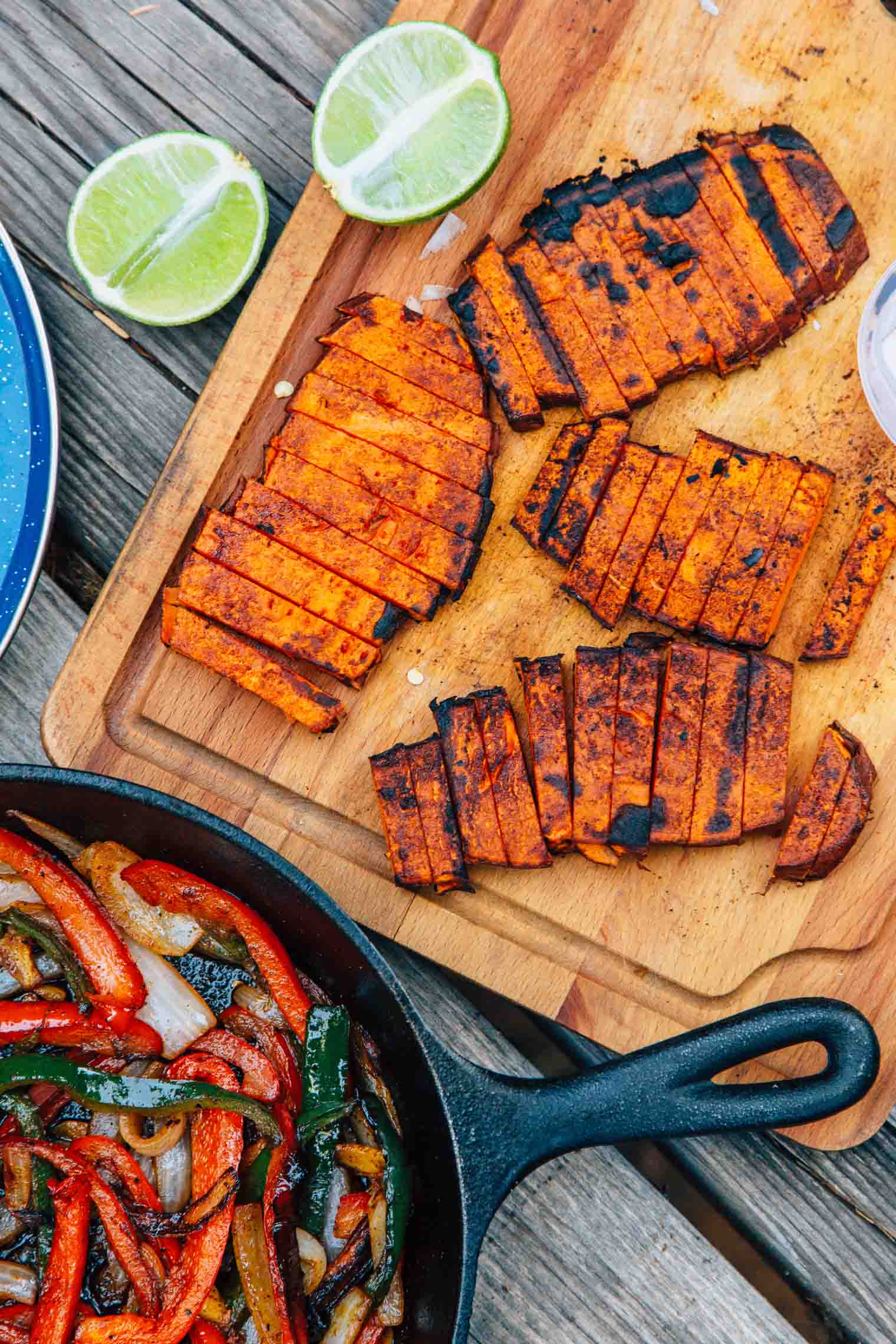 Grilled sweet potatoes on a wooden cutting board next to a cast iron skillet