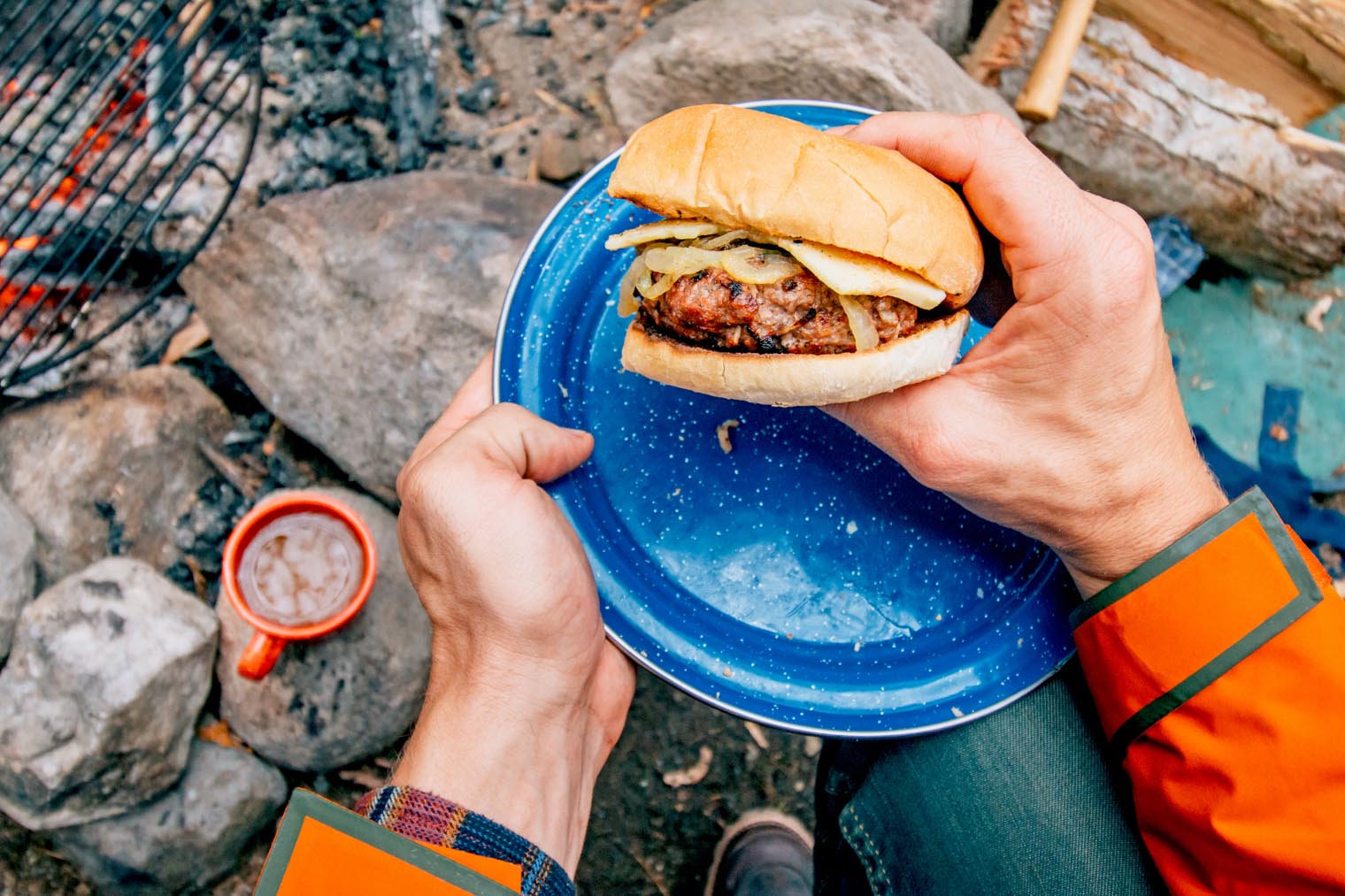 Apple cheddar burger on a blue camping plate in front of a campfire.
