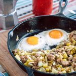Sausage and fennel hash with two eggs in a cast iron skillet Next to a cup of coffee