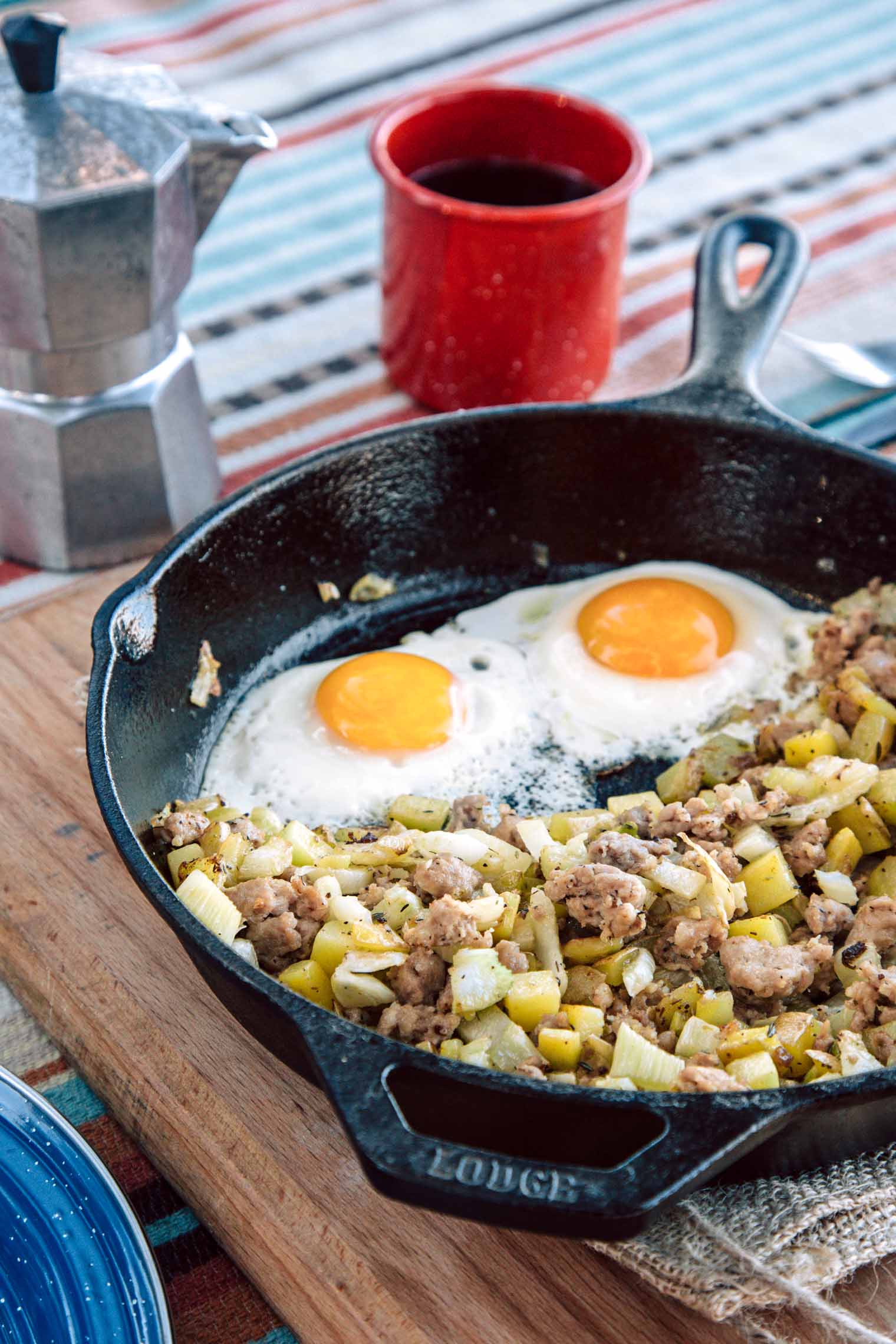 Sausage and fennel hash with two eggs in a cast iron skillet Next to a cup of coffee