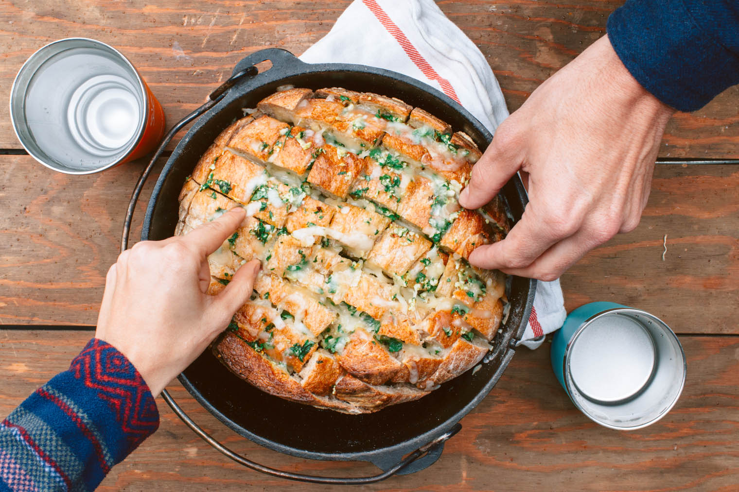 Two hands picking up  pieces of pull apart garlic bread in a Dutch oven