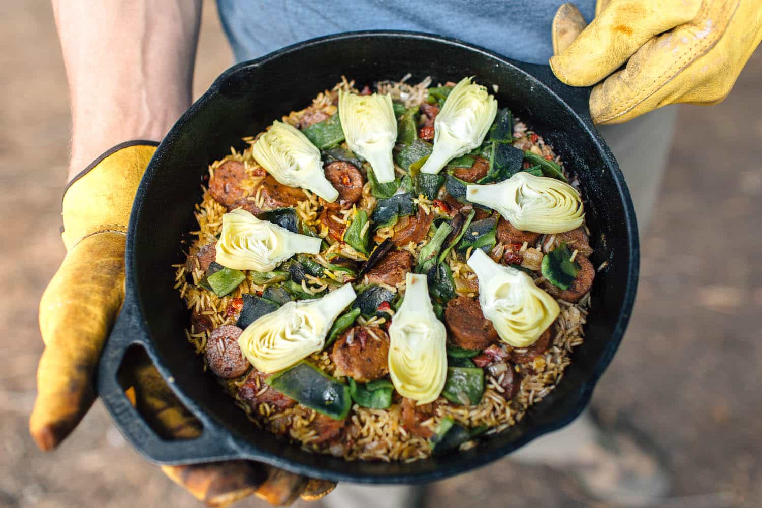 Michael holding a cast iron skillet filled with paella that is topped with artichoke hearts