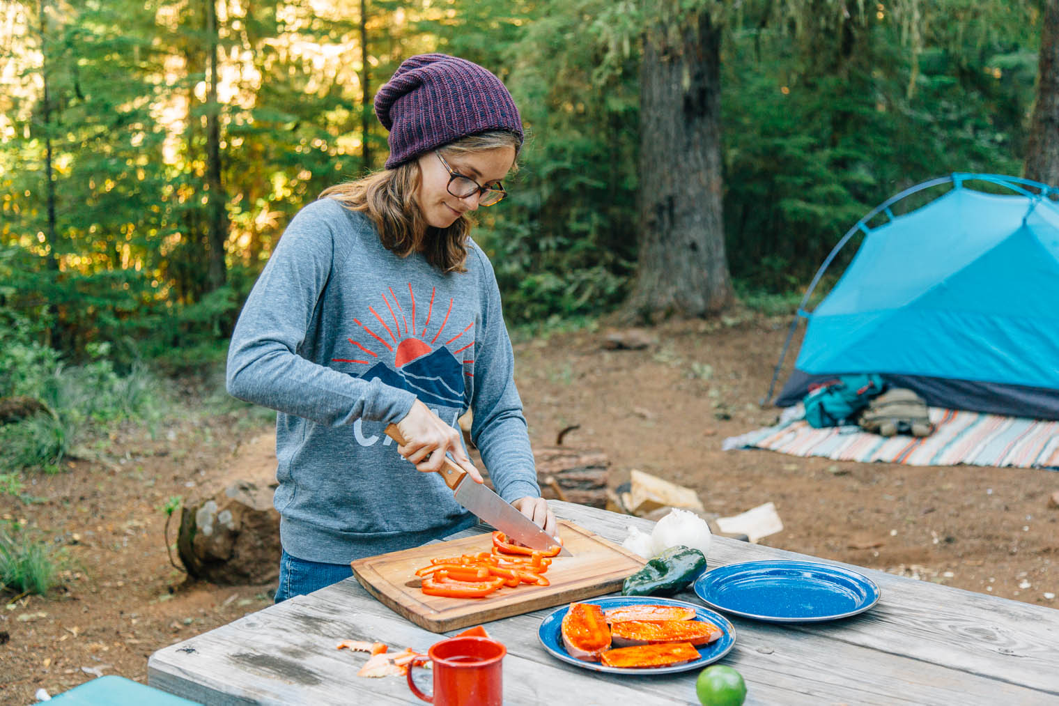 Megan standing at a camp table chopping red bell peppers on a wooden cutting board