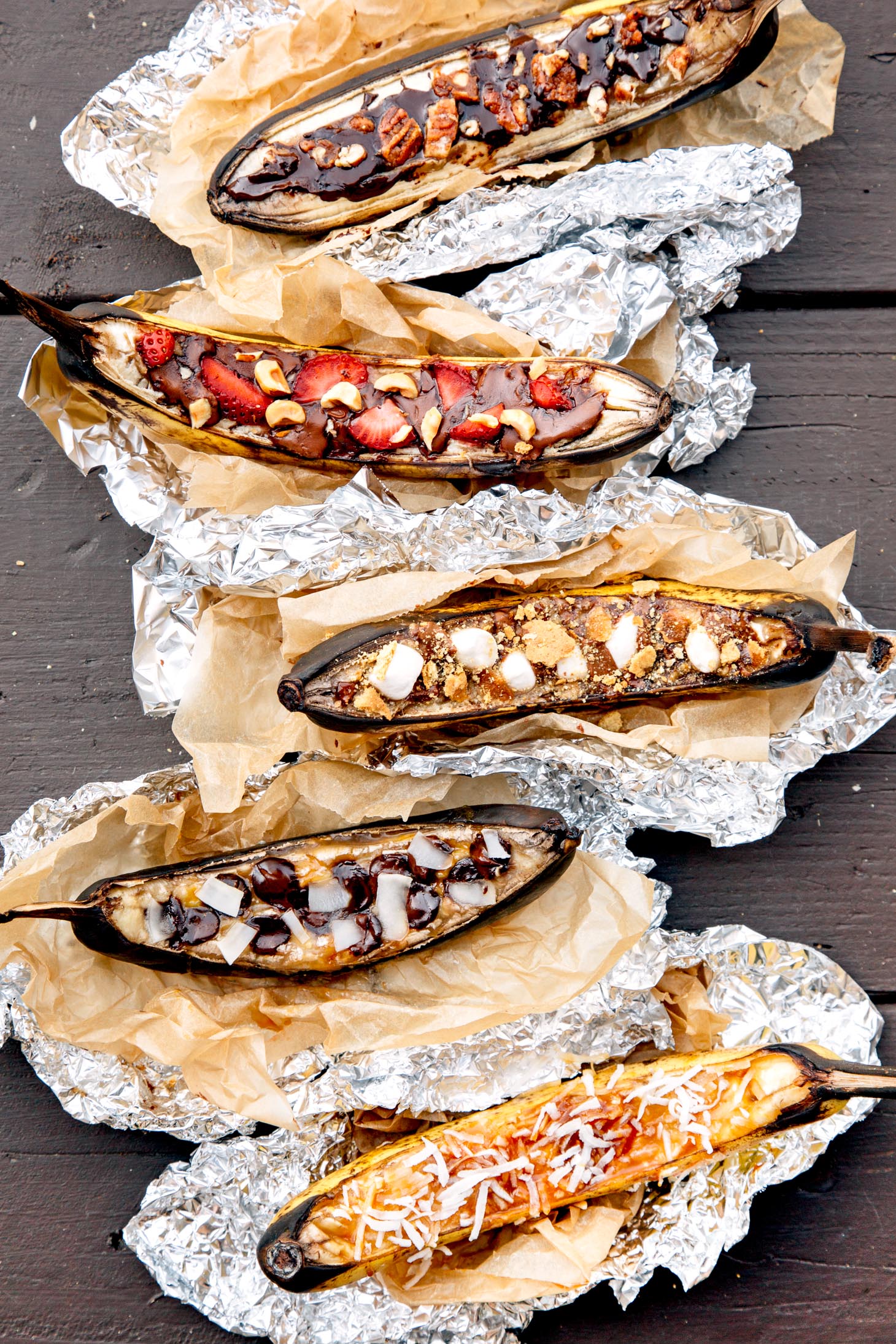 5 different campfire banana boats in foil lined up on a camping table