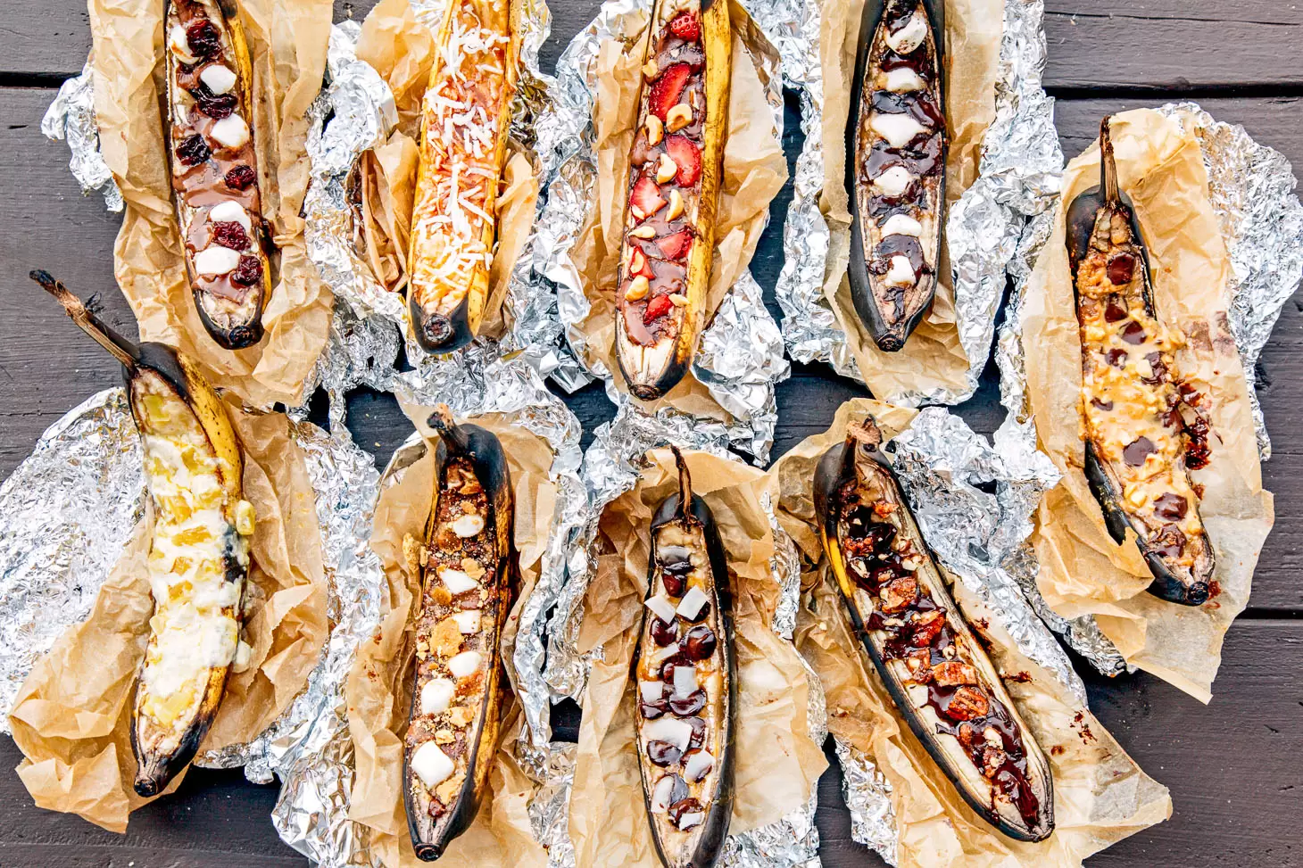 9 different campfire banana boats in foil lined up on a camping table