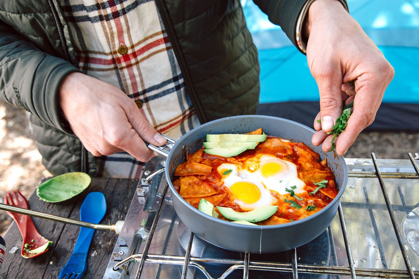 Michael is sprinkling chopped cilantro into a skillet full of Chilaquiles