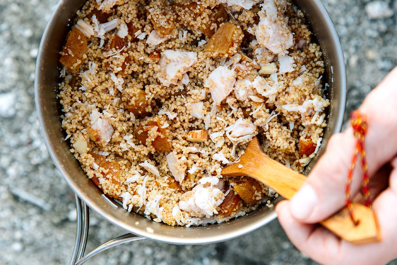 A hand holding a spoon scooping Moroccan chicken couscous out of a backpacking pot