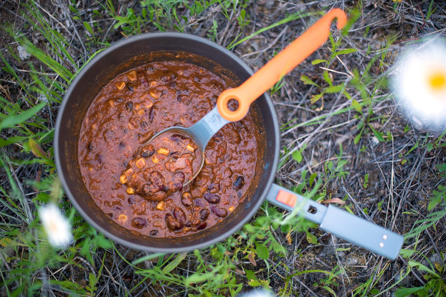 A backpacking pot filled with quinoa chili sitting on a grassy surface