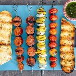 Grilled chorizo and vegetable kebabs on a blue cutting board