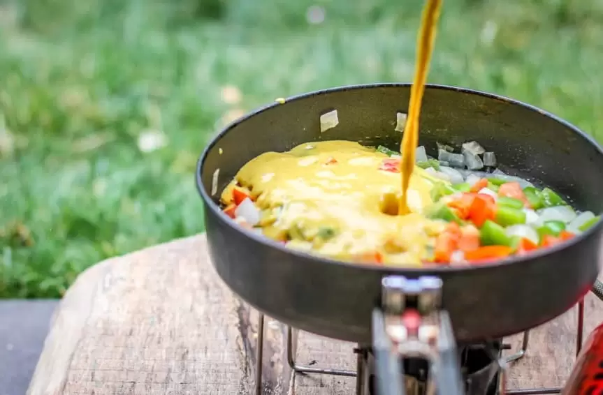 Pouring chickpea scramble mix into a camp frying pan.