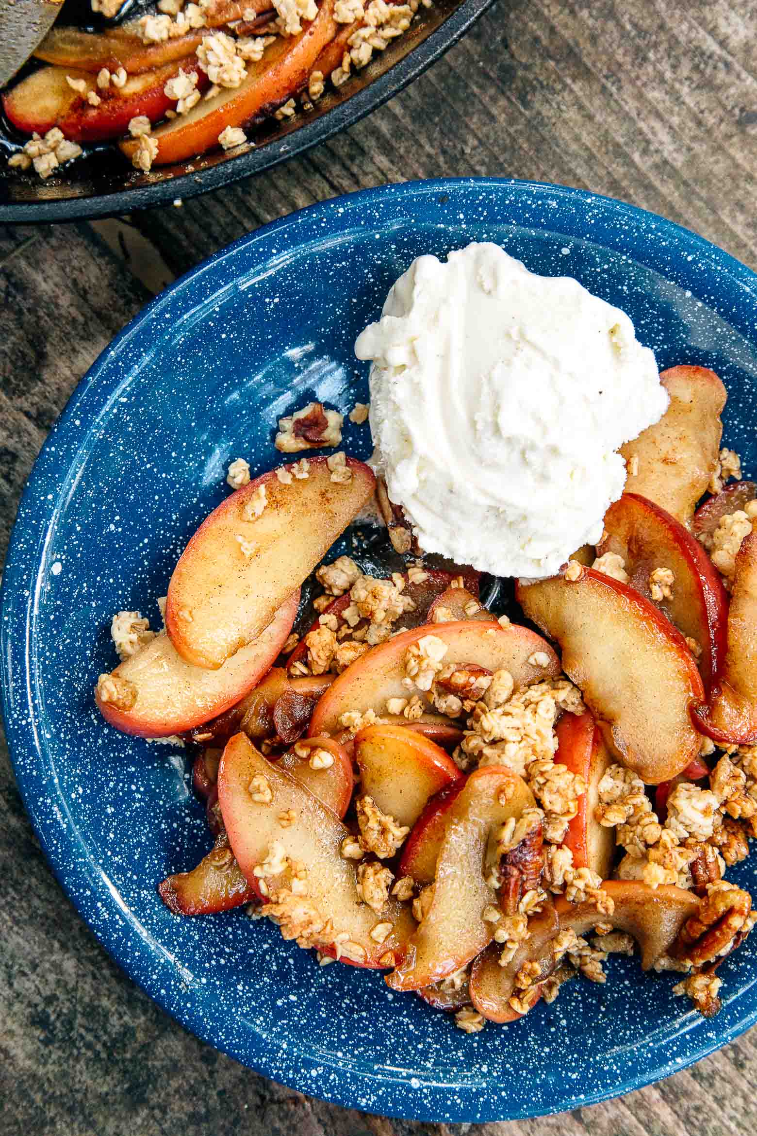 Apple crisp in a blue camping bowl with whipped cream