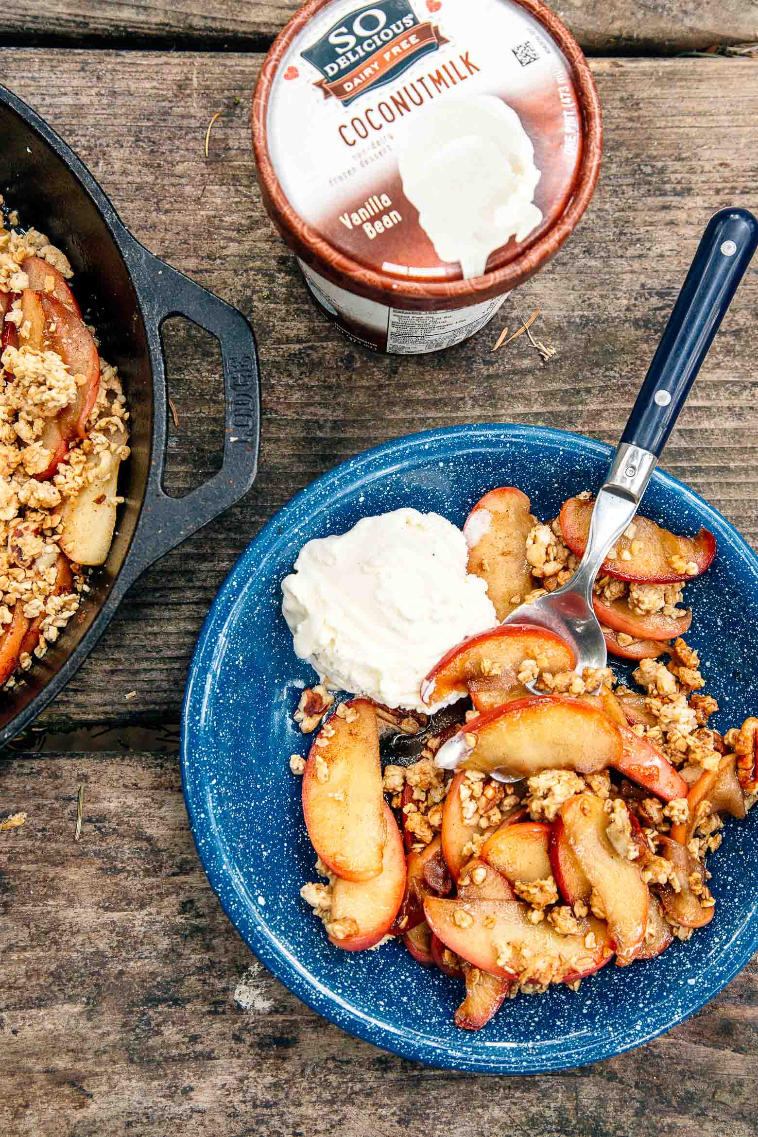 Apple crisp in a blue camping bowl with a scoop of ice cream.