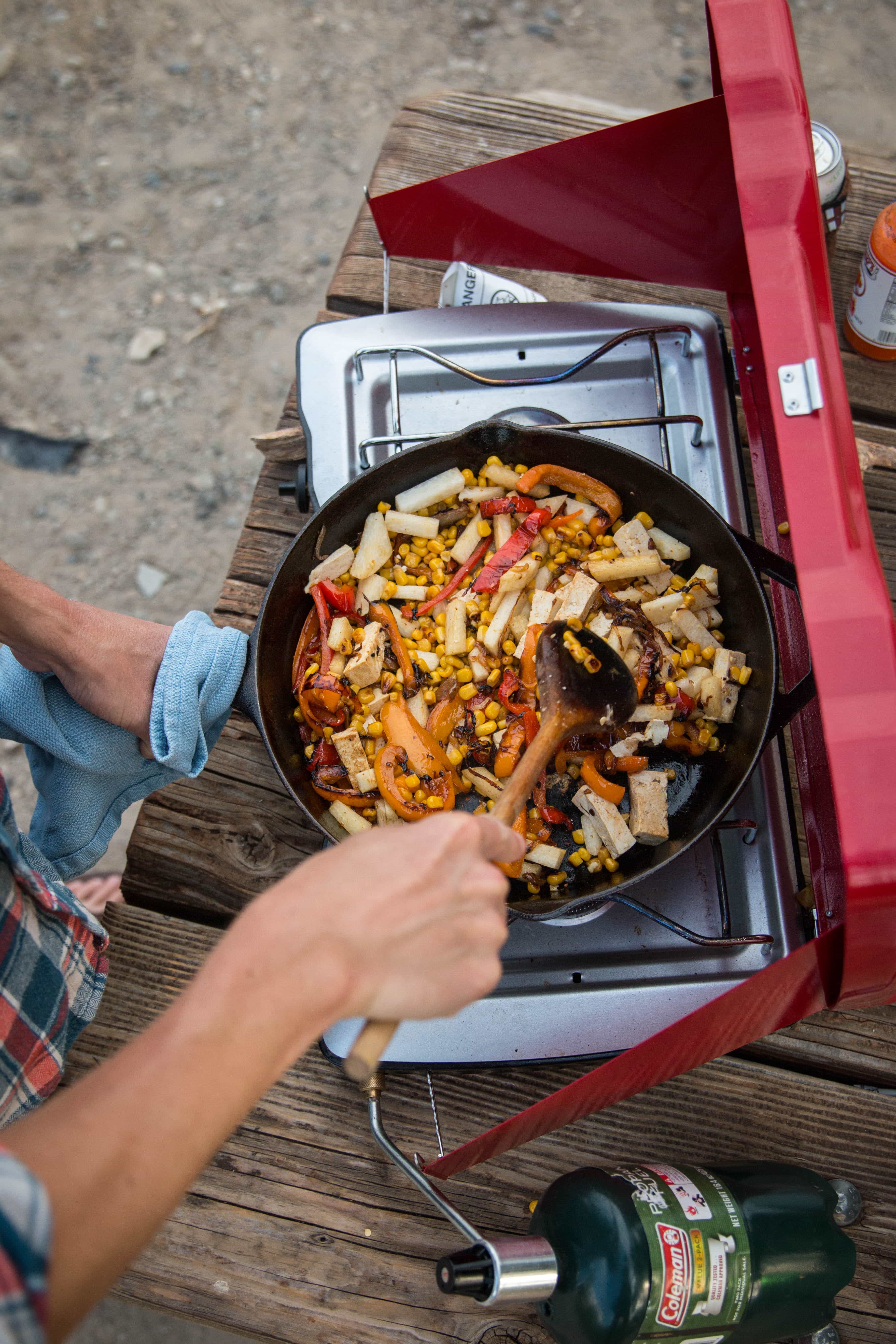 A man cooking stirfry udon noodles in a pan on a camp stove