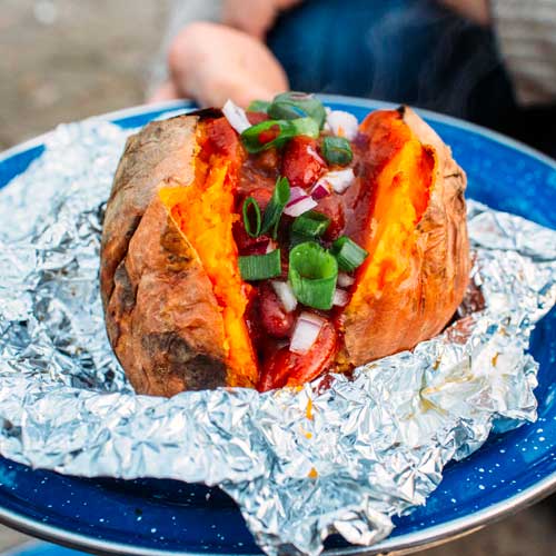 A blue plate with a sweet potato and chili in foil