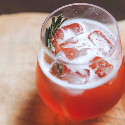 A glass of plum prosecco spritz with a sprig of rosemary