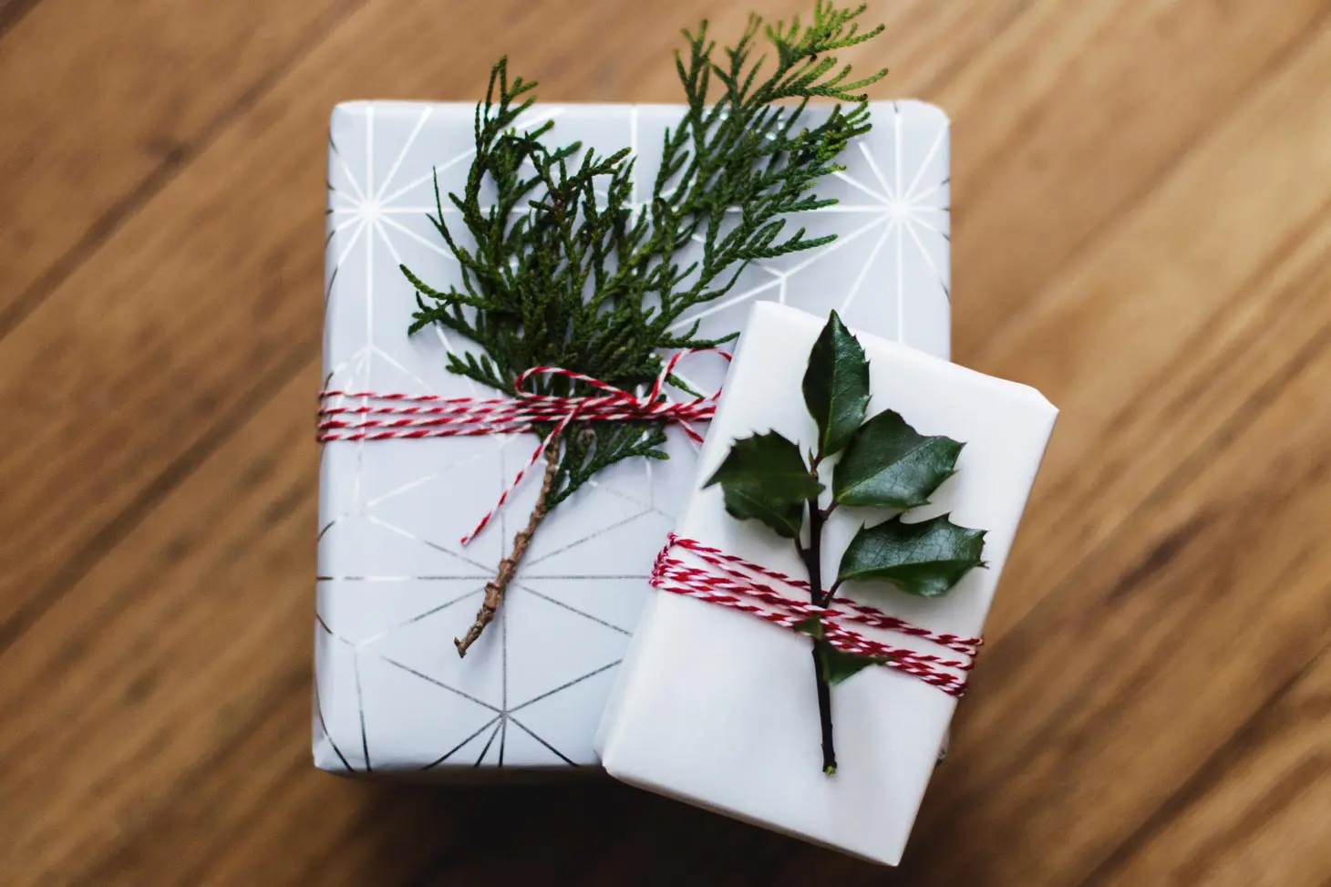 Two boxes wrapped in white paper with red ribbons and holly branches.